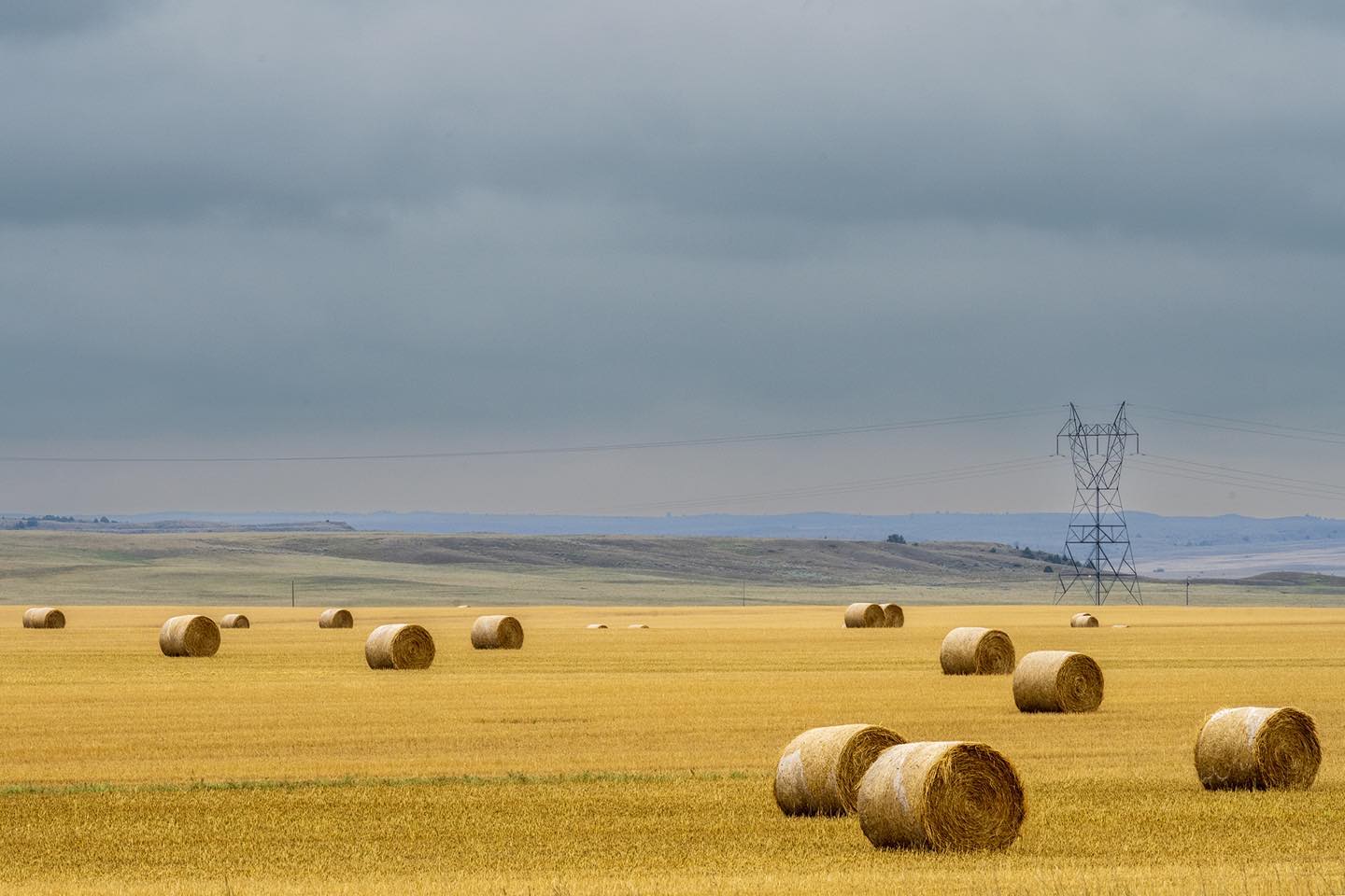 Hay rolls and a power line tower in Hathaway, Montana articulate the agricultural landscape in eastern Montana. The man-made objects are symbols of the economy in the Northern Great Plains. #hayrolls #hathawaymontana #northerngreatplains #montanaphotography